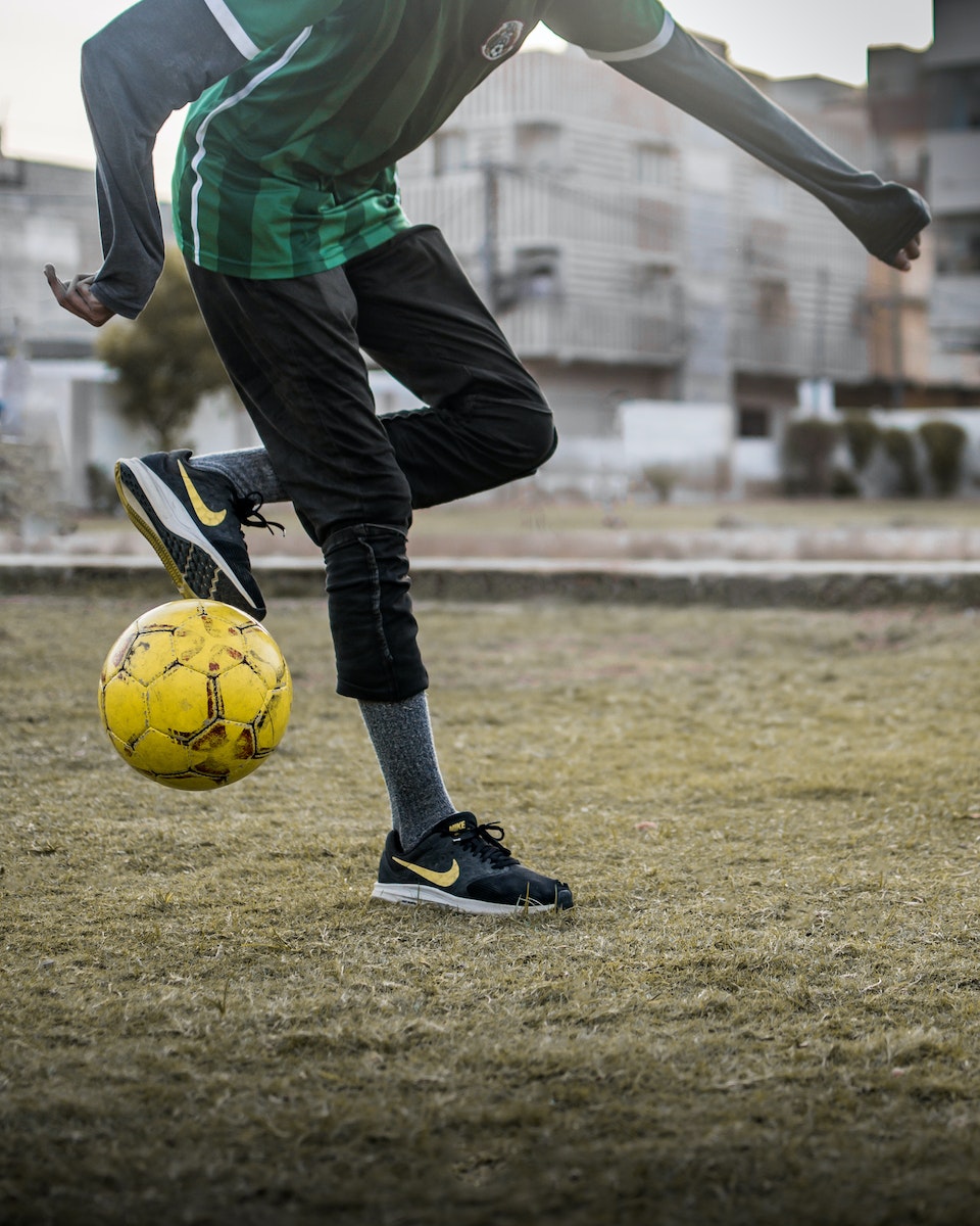 Crop sportsman kicking soccer ball on grass field in city